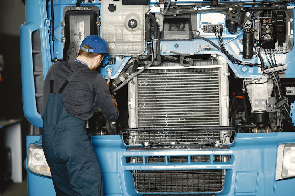 man in black uniform and blue cap fixing blue truck