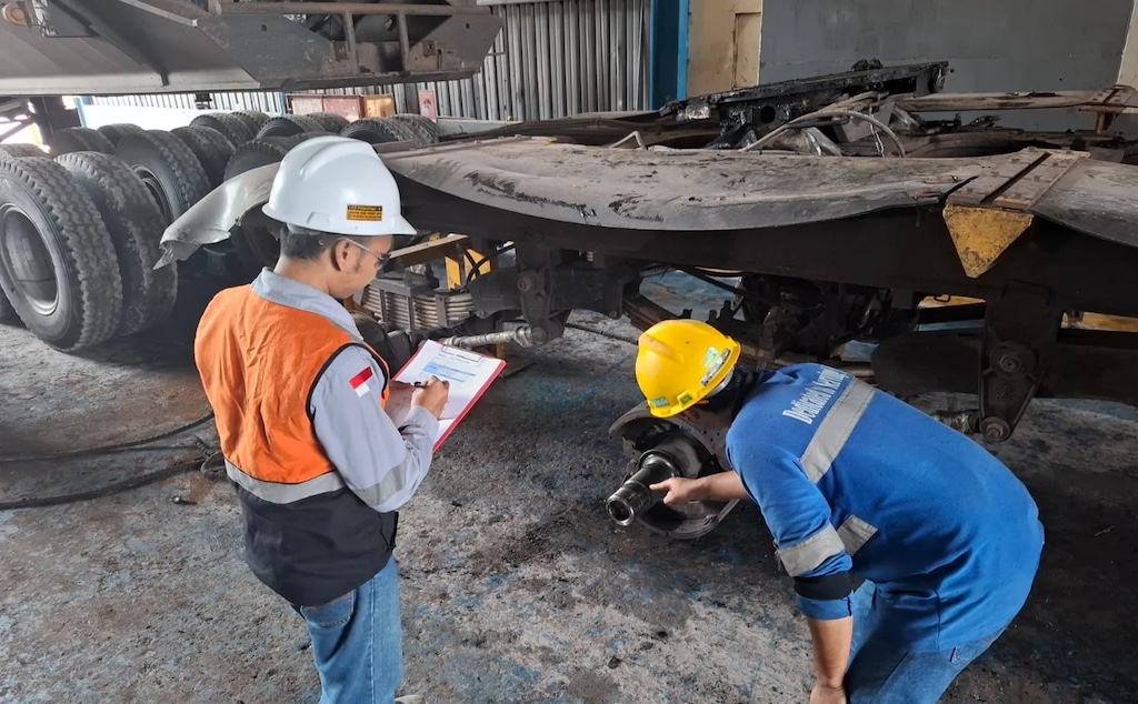 Teknisi melakukan inspeksi komponen axle trailer sambil mendokumentasikan hasil pemeriksaan di workshop. (Sumber Foto: TDU)