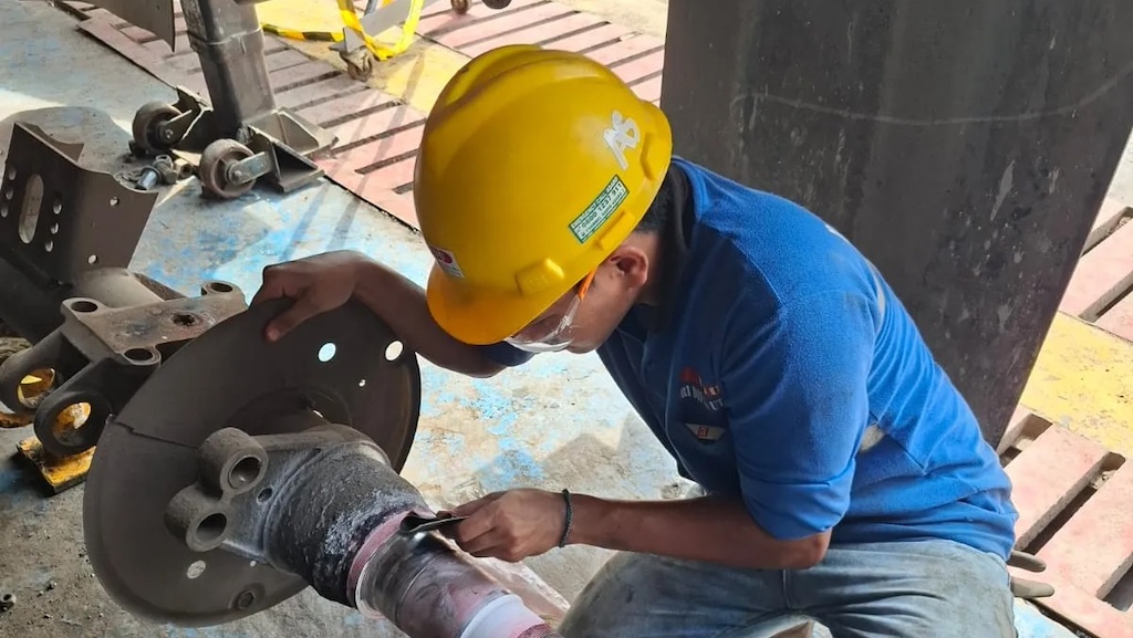 Teknisi memeriksa komponen axle trailer menggunakan alat inspeksi di workshop perawatan alat berat (Sumber Foto: TDU)